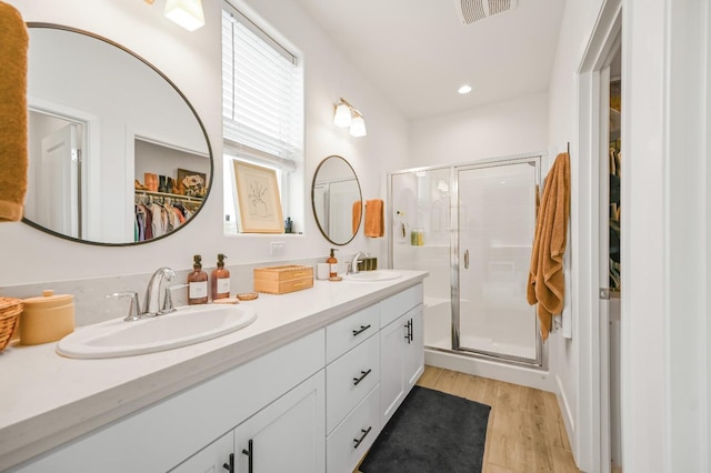 full bath with a spacious closet, a shower stall, wood finished floors, and a sink