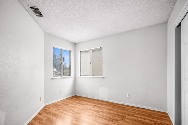 unfurnished room with baseboards, visible vents, light wood finished floors, and a textured ceiling