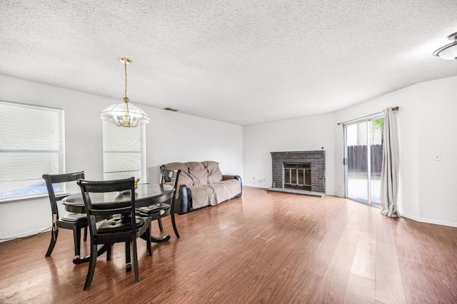 dining area featuring visible vents, a notable chandelier, a textured ceiling, wood finished floors, and a fireplace