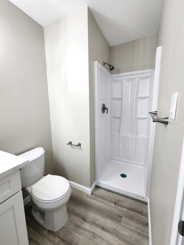 bathroom with baseboards, toilet, wood finished floors, vanity, and a shower