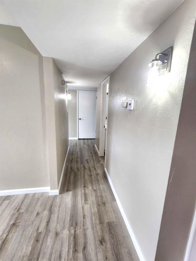 corridor with wood finished floors, baseboards, and a textured wall