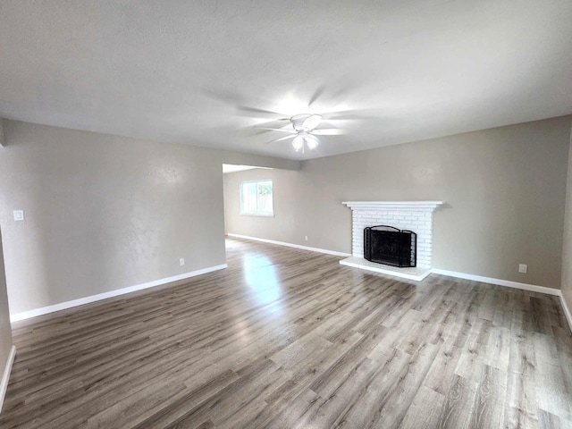 unfurnished living room featuring a brick fireplace, baseboards, a ceiling fan, and wood finished floors