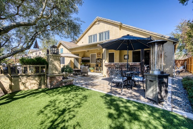 rear view of house featuring outdoor dining space, fence, stucco siding, a patio area, and a lawn