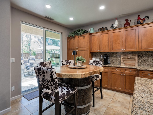 kitchen featuring light tile patterned floors, visible vents, brown cabinets, and backsplash