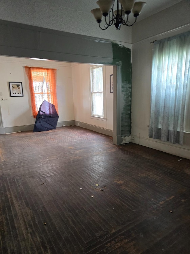 unfurnished room with baseboards, plenty of natural light, dark wood-type flooring, and an inviting chandelier