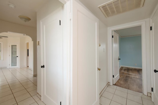 corridor with light tile patterned floors, arched walkways, visible vents, and baseboards