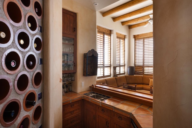 interior space featuring beamed ceiling, tile countertops, brown cabinets, and a sink