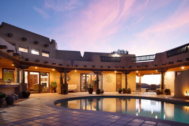 pool at dusk with a patio area and an outdoor pool