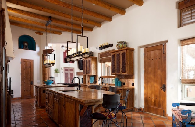 kitchen featuring beam ceiling, dark tile patterned flooring, an island with sink, a sink, and backsplash