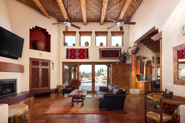 tiled living area with beamed ceiling, a warm lit fireplace, wooden ceiling, and a towering ceiling