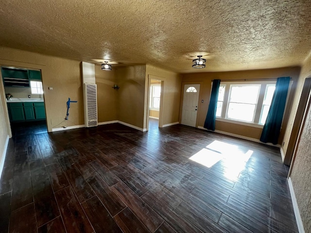 unfurnished living room featuring dark wood-style floors, baseboards, and a textured ceiling