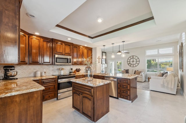 kitchen with light stone countertops, a peninsula, appliances with stainless steel finishes, a raised ceiling, and open floor plan