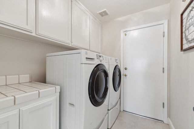 clothes washing area featuring washer and dryer, visible vents, and cabinet space