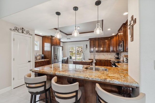 kitchen with backsplash, appliances with stainless steel finishes, a peninsula, a raised ceiling, and a sink