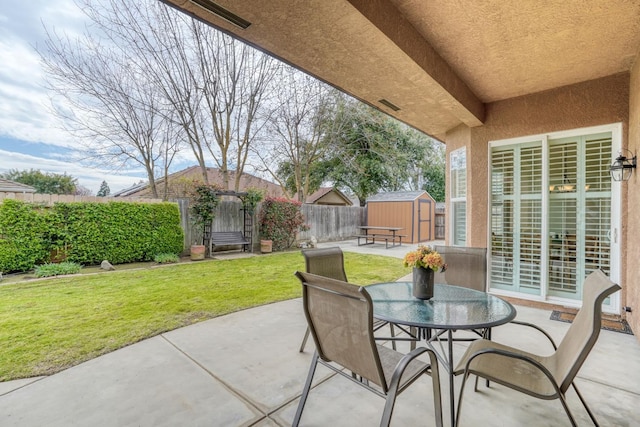 view of patio / terrace with a fenced backyard, outdoor dining space, a storage unit, and an outdoor structure