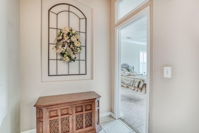 hallway with light tile patterned floors, visible vents, baseboards, ornamental molding, and light carpet