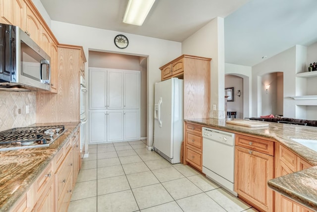 kitchen with light stone countertops, light tile patterned flooring, arched walkways, decorative backsplash, and appliances with stainless steel finishes