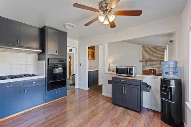 kitchen featuring stainless steel microwave, black oven, ceiling fan, under cabinet range hood, and a warming drawer