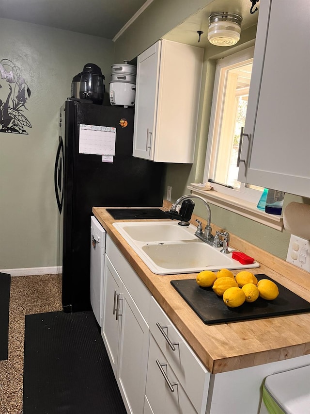 kitchen with baseboards, butcher block countertops, white cabinets, black electric cooktop, and a sink