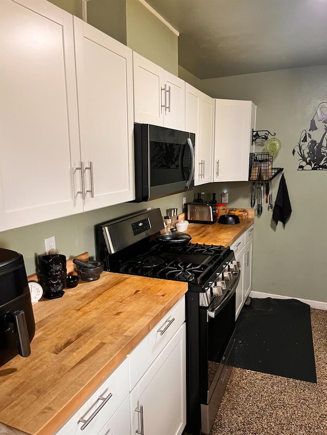 kitchen featuring baseboards, stainless steel gas stove, butcher block countertops, and white cabinets