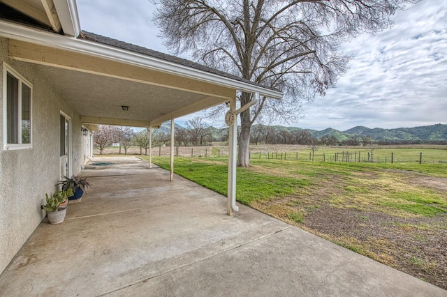 view of patio / terrace with a rural view, a carport, fence, and a mountain view