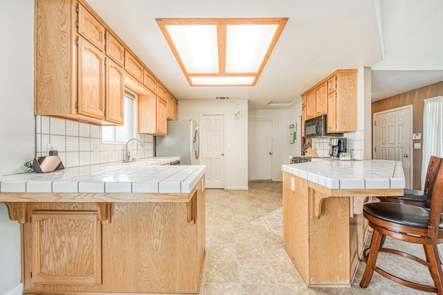 kitchen with tile counters, a peninsula, and stainless steel fridge