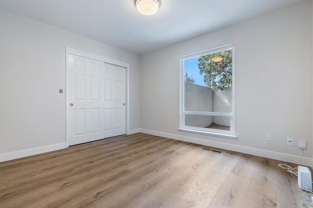 unfurnished bedroom with wood finished floors, visible vents, a closet, and baseboards