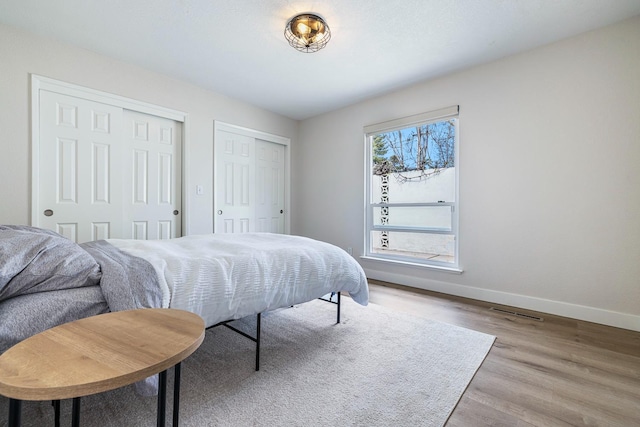 bedroom featuring visible vents, baseboards, two closets, and wood finished floors