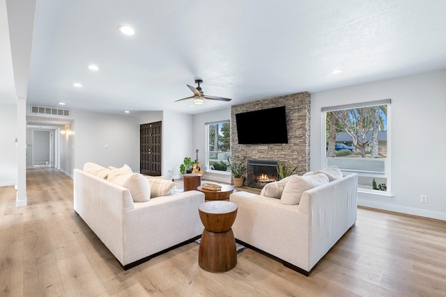 living area featuring visible vents, a stone fireplace, light wood-style flooring, and a ceiling fan