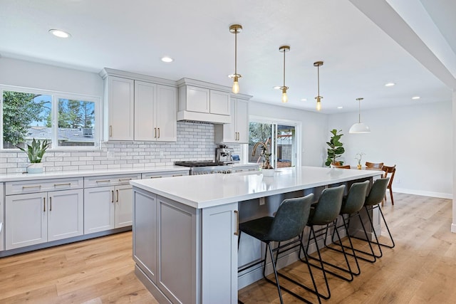 kitchen featuring light countertops, tasteful backsplash, light wood finished floors, and a center island with sink