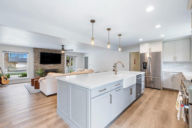 kitchen with light wood finished floors, backsplash, ceiling fan, stainless steel appliances, and a sink