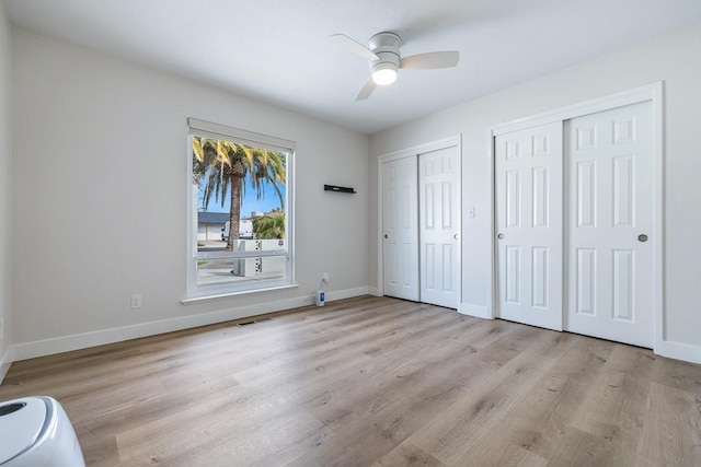 unfurnished bedroom featuring visible vents, baseboards, multiple closets, and wood finished floors