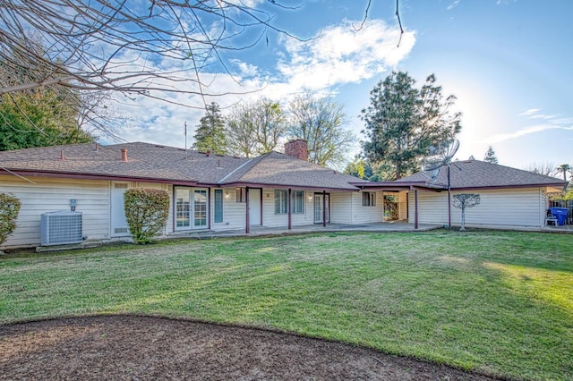 rear view of house featuring a chimney, central AC unit, and a lawn