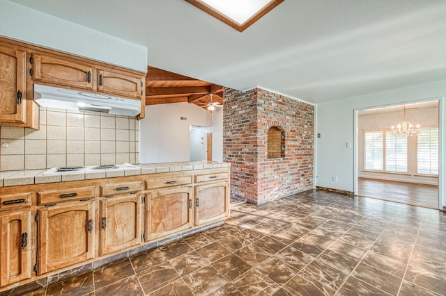 kitchen featuring tile countertops, lofted ceiling with beams, under cabinet range hood, white electric cooktop, and backsplash