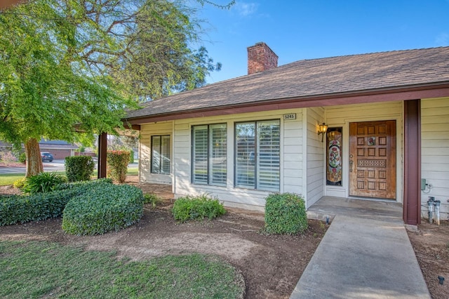 view of exterior entry with a porch, a chimney, and a shingled roof