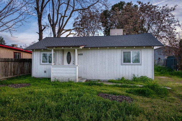 view of front of home with a shingled roof, a front lawn, and fence