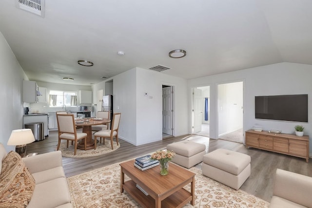 living room with vaulted ceiling, visible vents, and light wood-type flooring