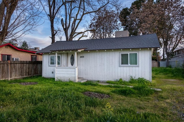 bungalow-style home with a front yard, fence, and a shingled roof