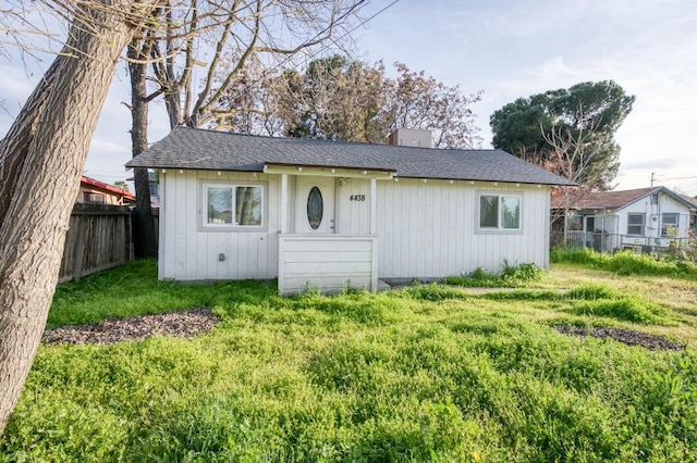 view of front of property with a shingled roof, a chimney, a front yard, and fence