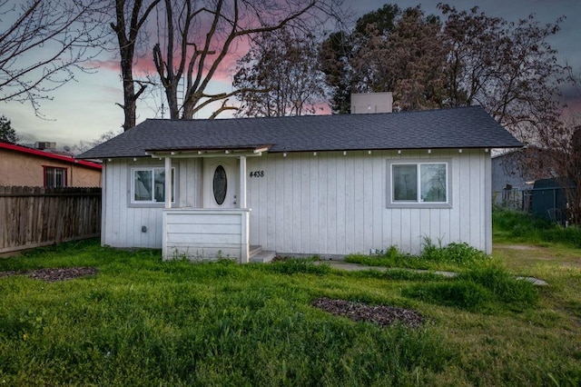 view of front facade with a front yard, fence, and roof with shingles