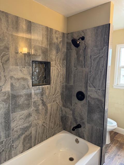 bathroom featuring shower / washtub combination, toilet, baseboards, and wood finished floors