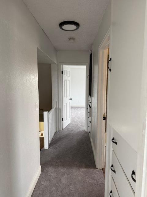 hall with baseboards, a textured ceiling, and carpet flooring