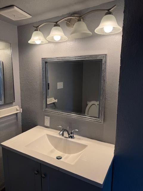 bathroom with visible vents, vanity, and a textured wall