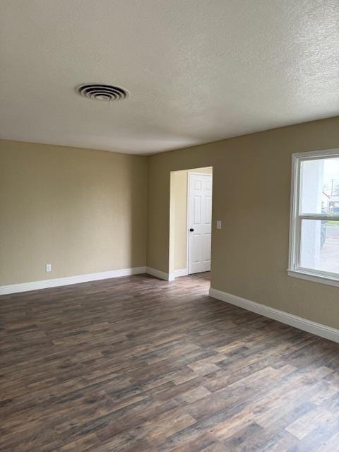 empty room with dark wood finished floors, baseboards, visible vents, and a textured ceiling