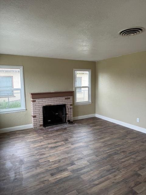 unfurnished living room with baseboards, visible vents, dark wood-style flooring, a textured ceiling, and a brick fireplace