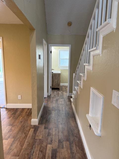 hall with stairway, a textured ceiling, baseboards, and dark wood-style flooring