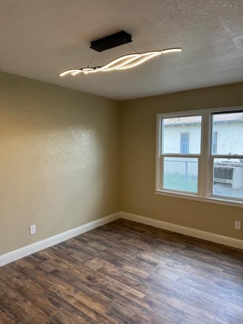 spare room with dark wood-style floors, a textured ceiling, and baseboards