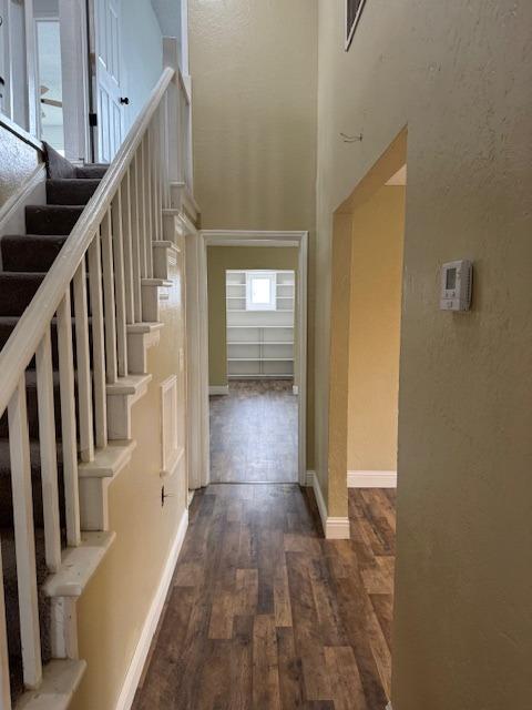 hallway featuring baseboards, dark wood-style floors, stairs, and a textured wall