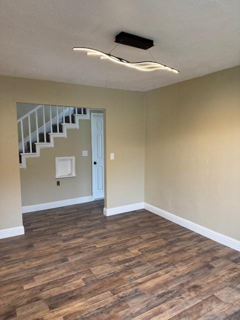 empty room with stairway, baseboards, dark wood-type flooring, and a textured ceiling