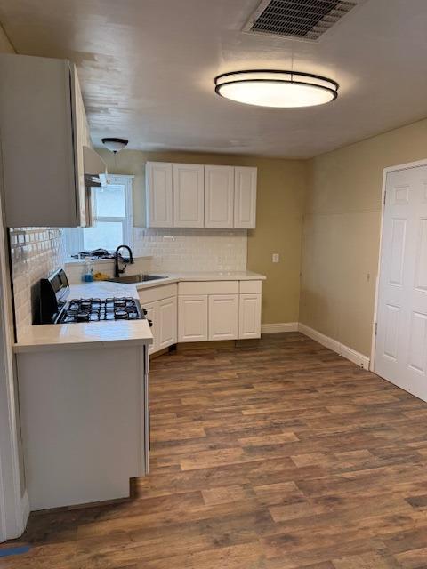 kitchen with visible vents, backsplash, gas stove, light countertops, and dark wood-style flooring